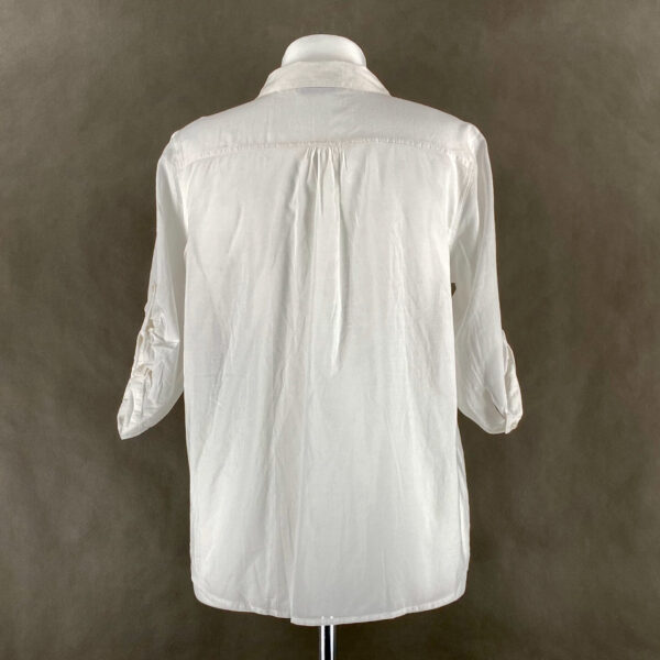 Biała koszula damska. Dekolt okrągły, rękawy sięgają za łokieć. Po obu stronach, na wysokości piersi - kieszenie. Koszula jest lekka, zwiewna, lekko oversize.