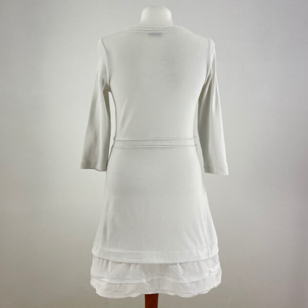 Biała sukienka z rękawami trzy czwarte. Dekolt okrągły. Lekko asymetryczny dół - z tyłu nieco wydłużony i zakończony delikatnymi falbankami. Sięga przed kolano. Wykonana z rozciągliwego materiału.
